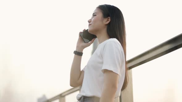 A business Asian woman in a white t-shirt is talking on the phone with friends.