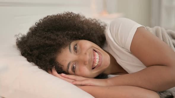 Young African Woman Laying in Bed Smiling at Camera