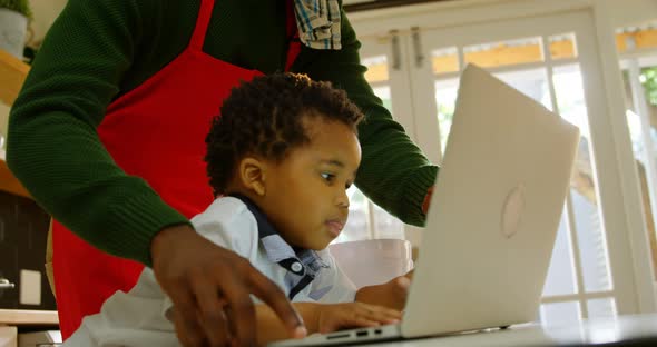 Low angle view of young black father and son using laptop in kitchen of comfortable home 4k