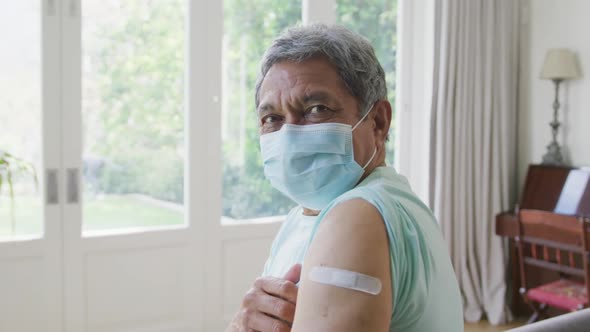 Portrait of senior man wearing protective face mask showing covid vaccine bandage on shoulder