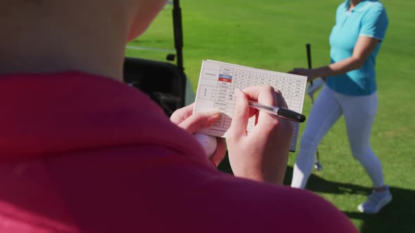 Two caucasian women playing golf one writing in a notebook