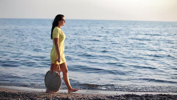 Smiling Pretty Woman in Yellow Dress Walking on Sea Shore at Sunset