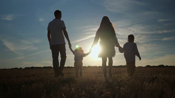 Family with Children Walks Along Fields at Back Setting Sun