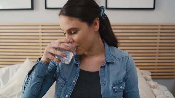 Front view on caucasian woman in advanced pregnancy sitting on bed and drinking water. Shot with RED