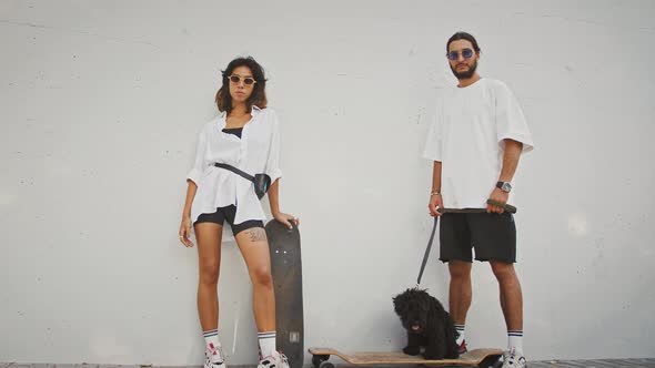 Portrait of Young Stylish Couple Posing with Skateboard and Dog Tracking Shot