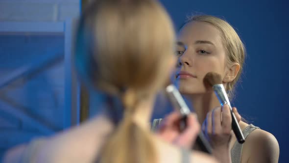 Smiling Young Woman Applying Face Powder and Making Kiss Gesture in Mirror