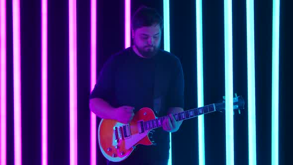The Guitarist Enjoys His Electric Guitar Playing in a Dark Studio Surrounded By Bright Blue and Pink