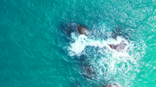 Foamy waves crashing on the boulders in the aquamarine sea. Tropical vacation background