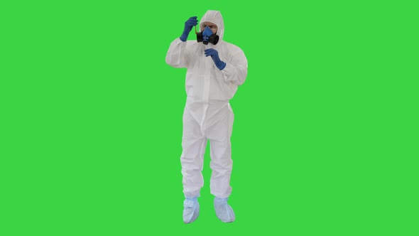 Doctor in Hazmat Suit and Gas Mask Holding Test Tube of Blood on a Green Screen, Chroma Key.