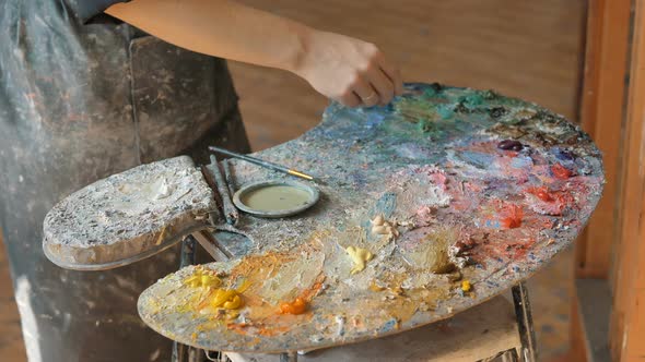 Artist in Dirty Apron Mixes Oil Paints on Palette in Studio