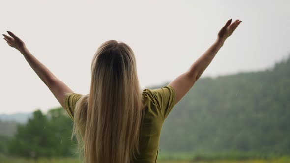 Woman Raise Hands Up Happy of Warm Rain Against Green Hill