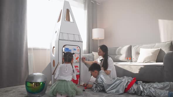 Asian Female with Her Kids Play in the Living Room at Home a Boy in an Astronaut Costume Lying on