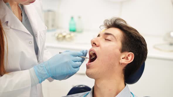 Young Male Patient During Oral Health Checkup and Visual Examination By Professional Female Dentist