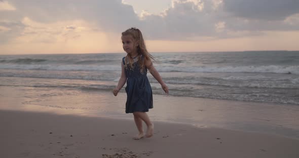 Little Girl Plays on the Beach Near the Water at the Sea Coast