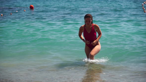 Young Woman with Long Hair in a Red Swimsuit and Bracelets in Boho Style Enjoying the Waves on the