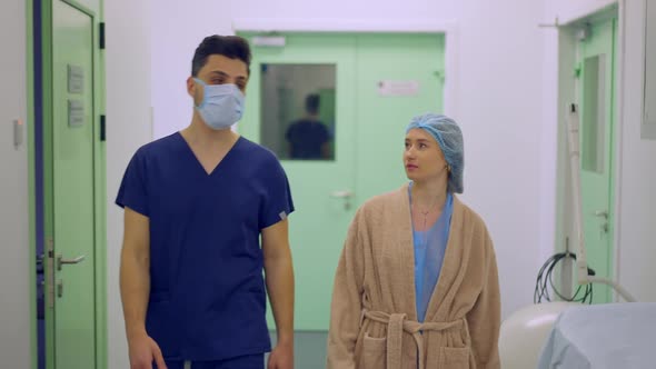 Medium Shot Portrait of Male Plastic Surgeon in Face Mask and Female Patient Walking in Slow Motion