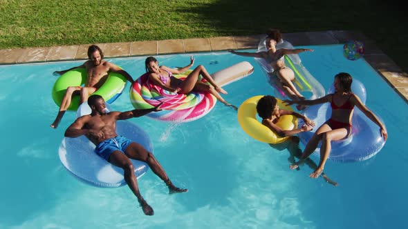 Diverse group of friends having fun playing on inflatables in swimming pool