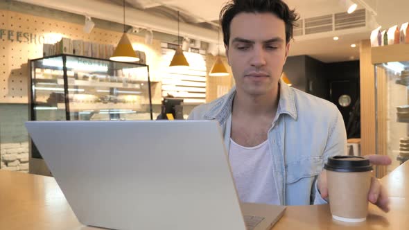 Young Man Drinking Coffee and Working on Laptop in Cafe