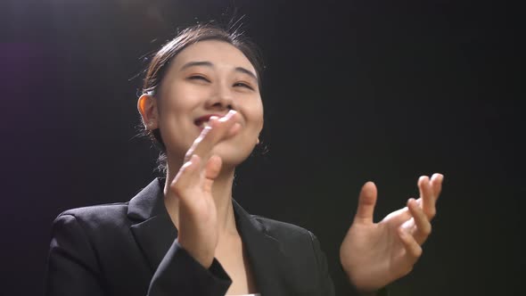 Smiling Speaker Woman In Business Suit Clapping Her Hands And Looking Around In The Black Studio