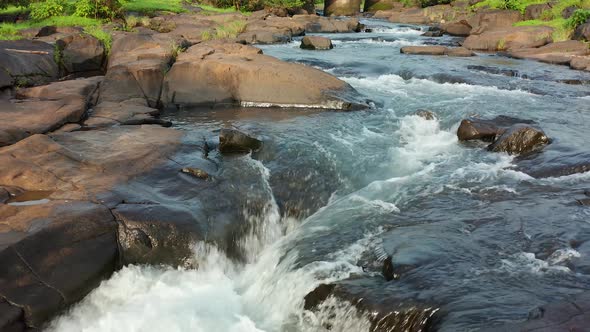 Camera following the clear water of the stream as it rushes over the stones to a waterfall