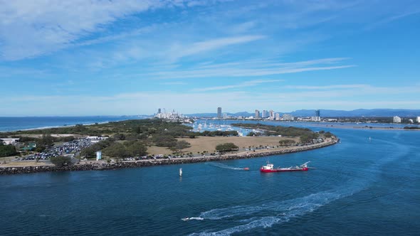 Large industrial ship positioned in a coastal ocean inlet with a urban skyline in the distance. High