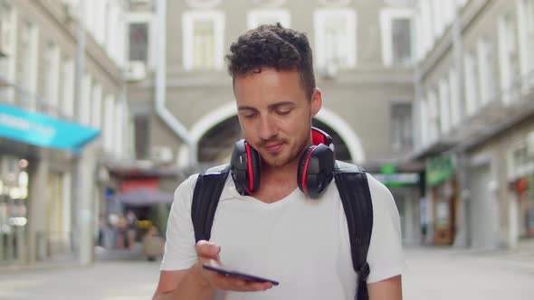 Portrait of Handsome Young Man Listening Music From His Smartphone in Red Headphones on Street of