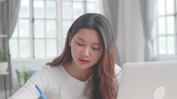 Asian Girl Using Laptop Computer And Writing On Notebook