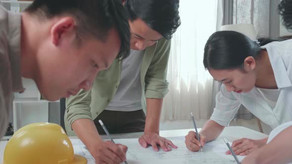 Group Of Asian Engineers Helping Each Other Drawing Building Construction At The Office