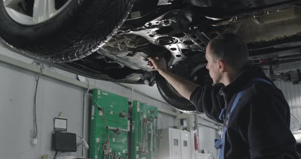 Auto Mechanic Working Under The Car In Dealer's Garage.