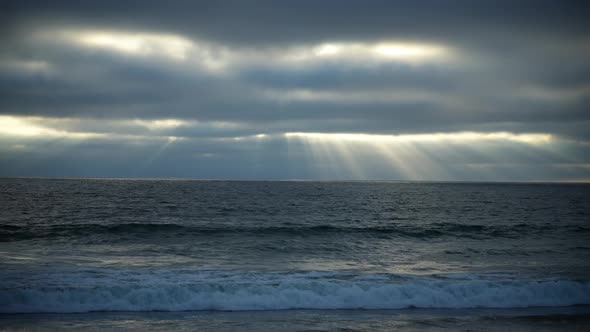 Heavens' rays shining through the clouds over the moody ocean landscape - static