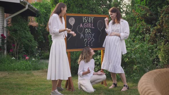 Wide Shot Cheerful Thoughtful Pregnant Woman and Girls Standing at Blackboard with Is It Boy or a