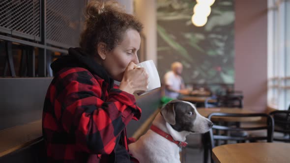 Side View of Young Woman Drinking Coffee and Hugging and Kissing Her Brown and White Adorable Dog 