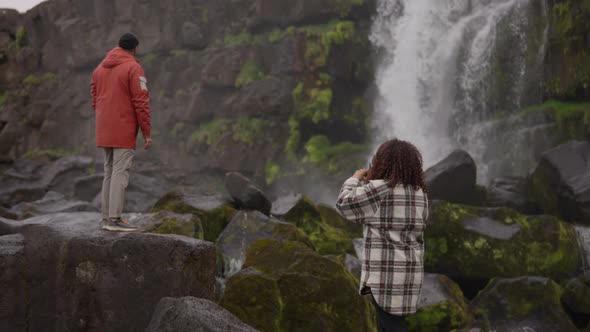 Woman Using Old Camera To Film Man Watching Oxararfoss Waterfall