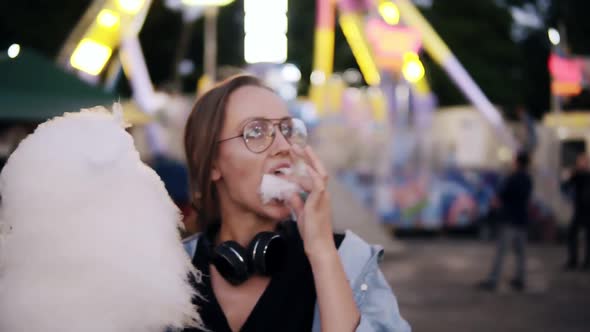 An Attractive Girl Walking in the Amusment Park Eats White Cotton Candy