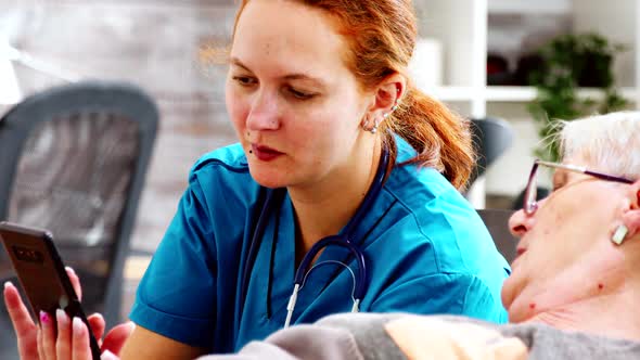 Close Up Shot of Nurse Helping an Elderly Disabled Woman To Use a Smartphone