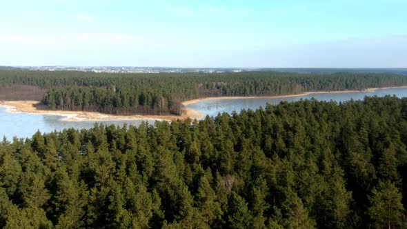 A zoomed in aerial view of an enourmous frozen lake and vast forest during winter season, Poland.