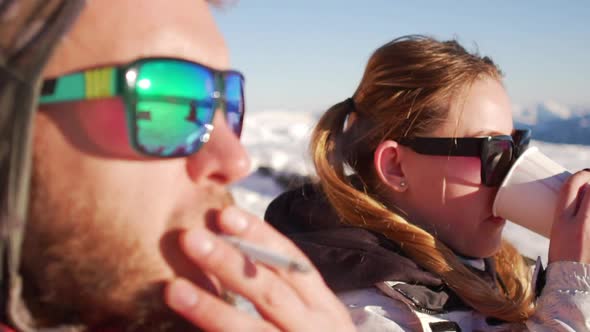 Close Up Footage in Slowmotion of Caucasian Male and Female in Sun Glasses Sitting on Ski Mountain