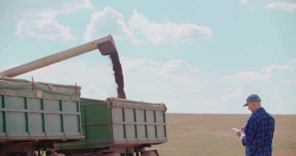 Farmer Using Digital Tablet While Looking at Tractor in Farm