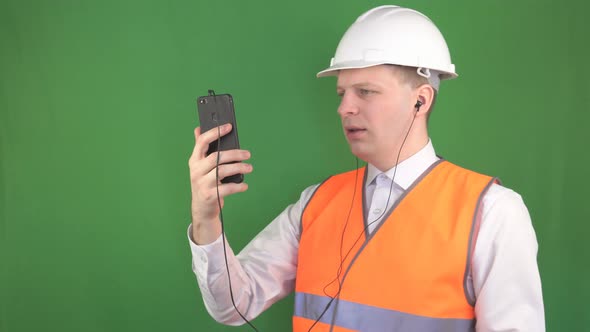 Young Caucasian Male Boss Talking on the Phone Video Call in Headphones at the Construction Site