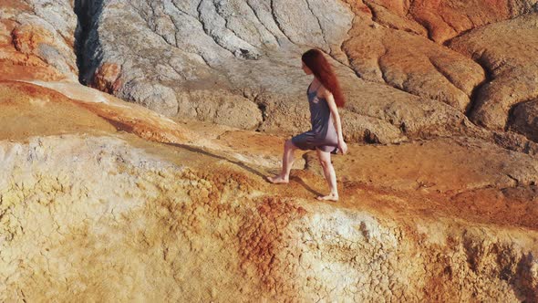 Aerial View of a Girl Who Climbs the Red Mountains in a Dress