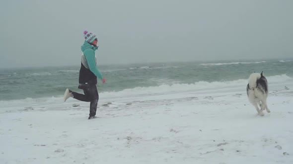 Young Female Playing and Runing with Siberian Husky Dog on the Beach at Snow Storm Slow Motion