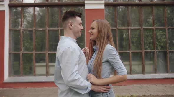 Young Couple in Love Dance Holding Hands Against the Background of Large Windows of a Building