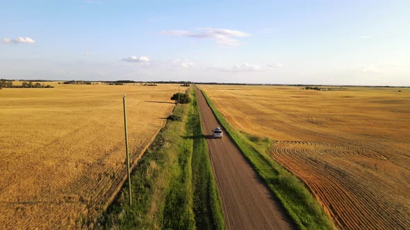 Silver Car driving along long telegraph dirt road in American countryside during sunset. Drone follo