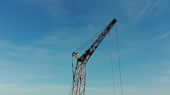 Two Construction Cranes on the Background of Blue Sky and the Sun Which Shines in the Camera Hiding