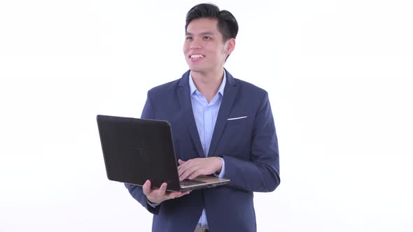 Happy Young Asian Businessman Thinking While Using Laptop