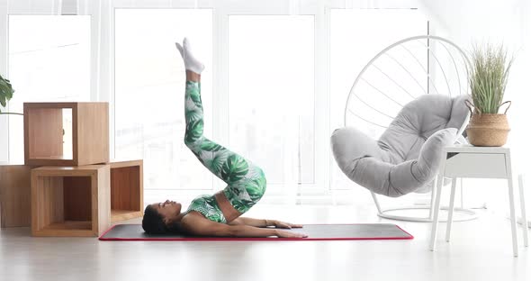 Sporty black woman is doing abs exercises on floor at home.