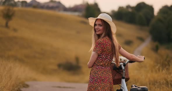 A Girl in a Hat with a Bicycle Turns Around and Looks at the Camera Smiling