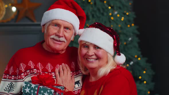 Senior Couple Family in Santa Claus Hats Celebrating Christmas Looking at Camera and Hugging at Home