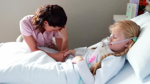 Sick girl in oxygen mask resting on bed