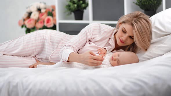 Adorable Young Mother Holding Hands Admiring Sleeping Toddler